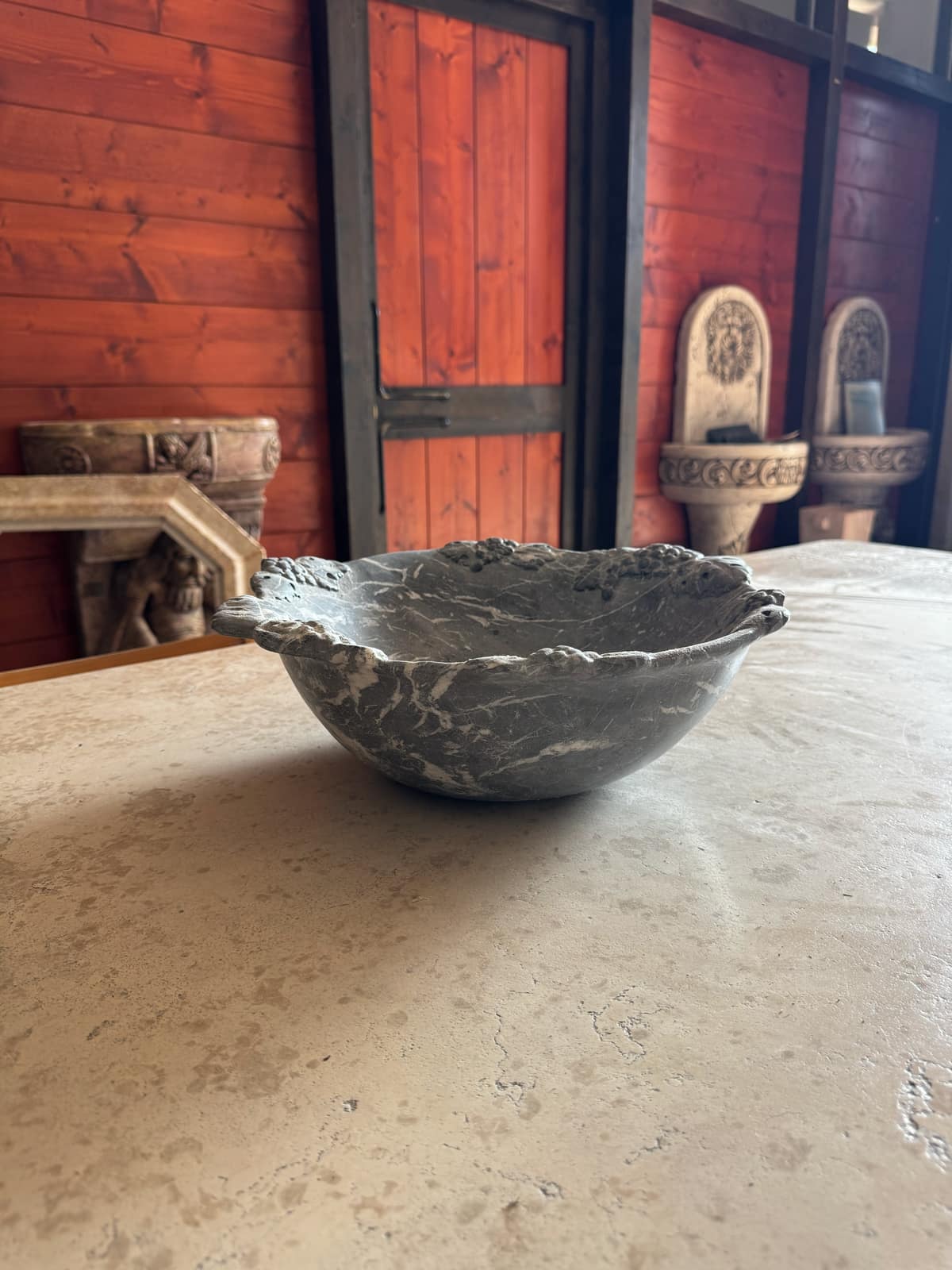 Vasca a forma di conchiglia in marmo grigio venato, appoggiata su un grande piano in travertino
