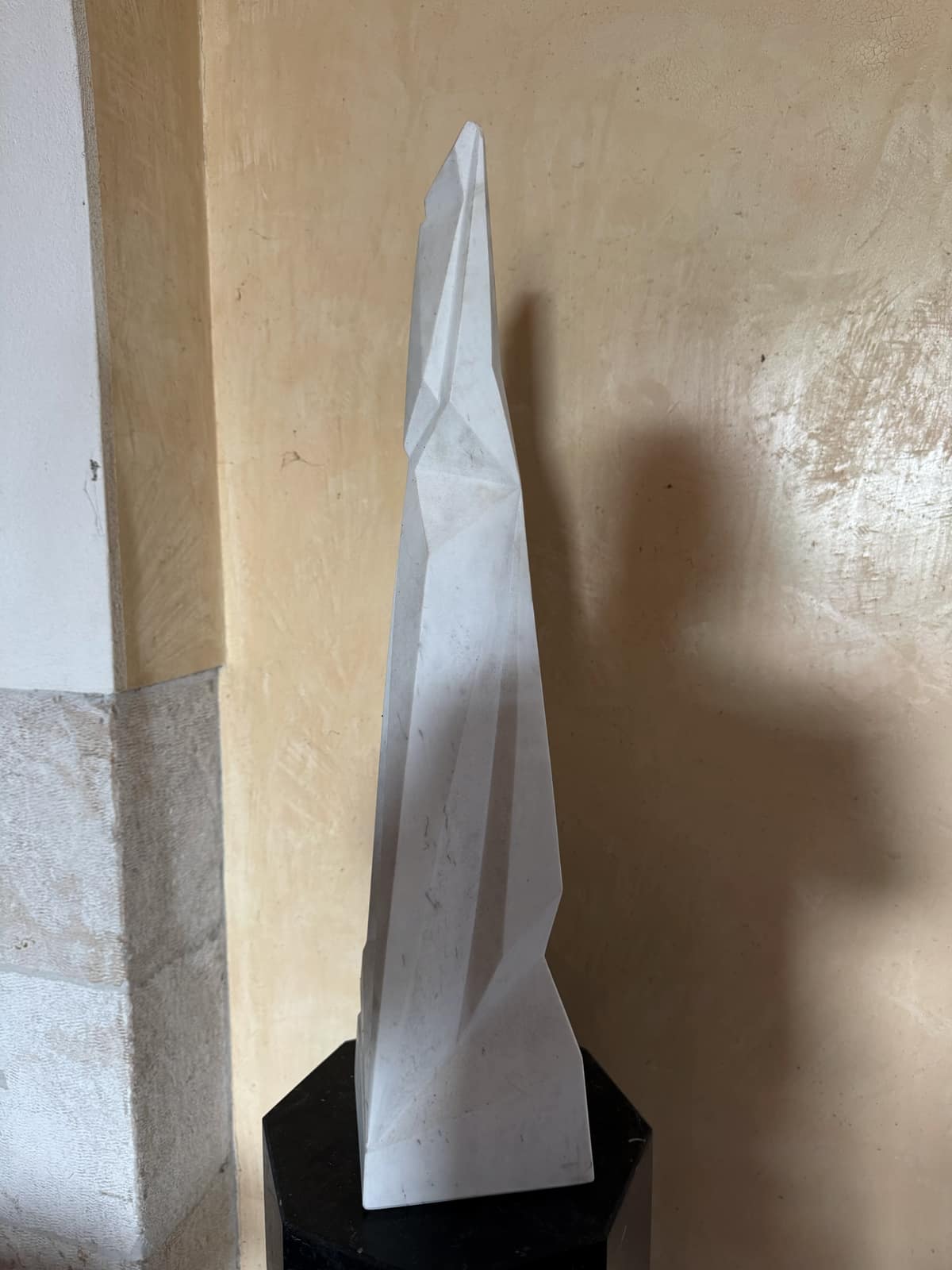 Scultura astratta contemporanea in marmo bianco dalle superfici sfaccettate, su base nera