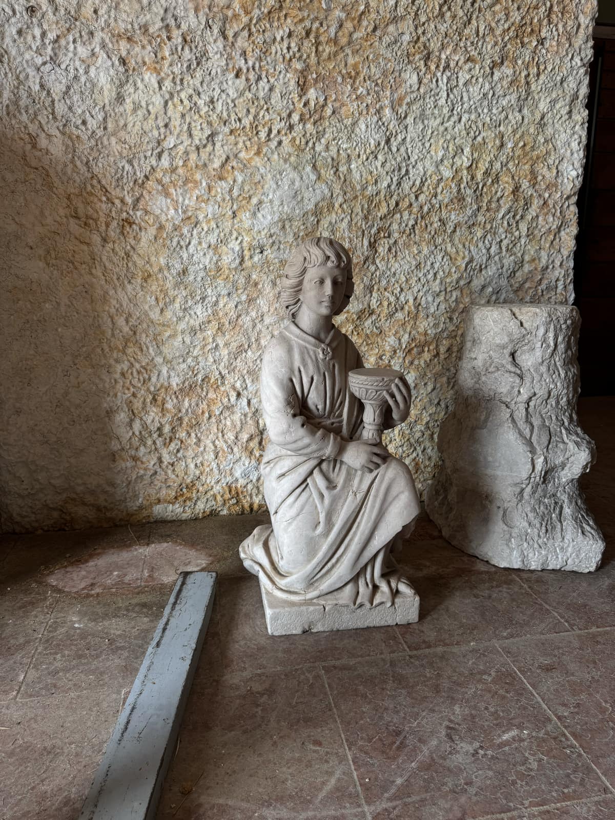 Statua classica di figura femminile panneggiata con anfora, davanti a una parete in pietra grezza